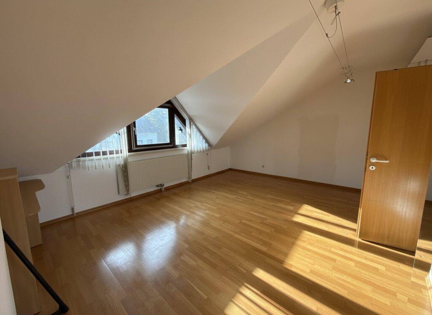 Leeres Schlafzimmer im Dachgeschoss mit Holzboden, Dachschräge und viel Tageslicht.