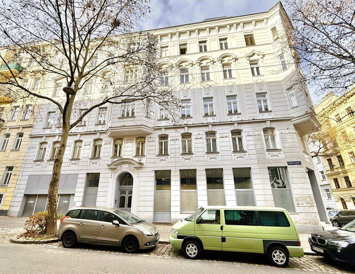 Historische Fassade eines Altbaus in einer städtischen Straße mit geparkten Fahrzeugen.