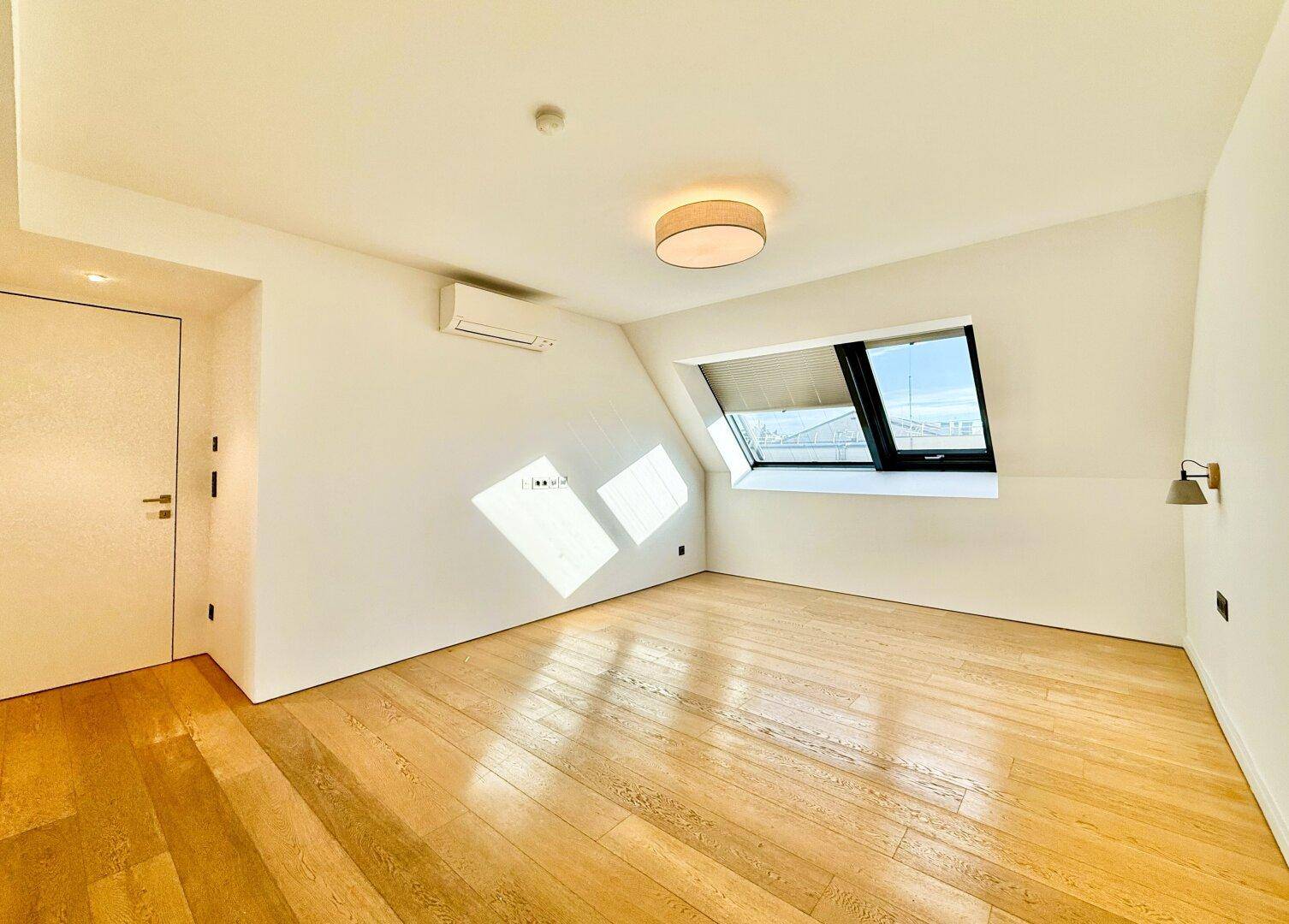 Leeres, helles Schlafzimmer mit Holzboden und Dachfenster, bietet viel Potenzial für individuelle Einrichtung.