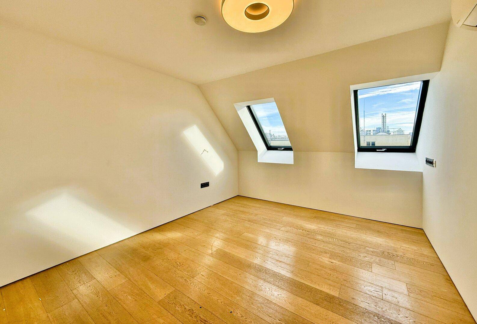 Leeres, helles Zimmer mit Holzboden und zwei Dachfenstern, bietet flexible Nutzung als Büro oder Schlafzimmer.
