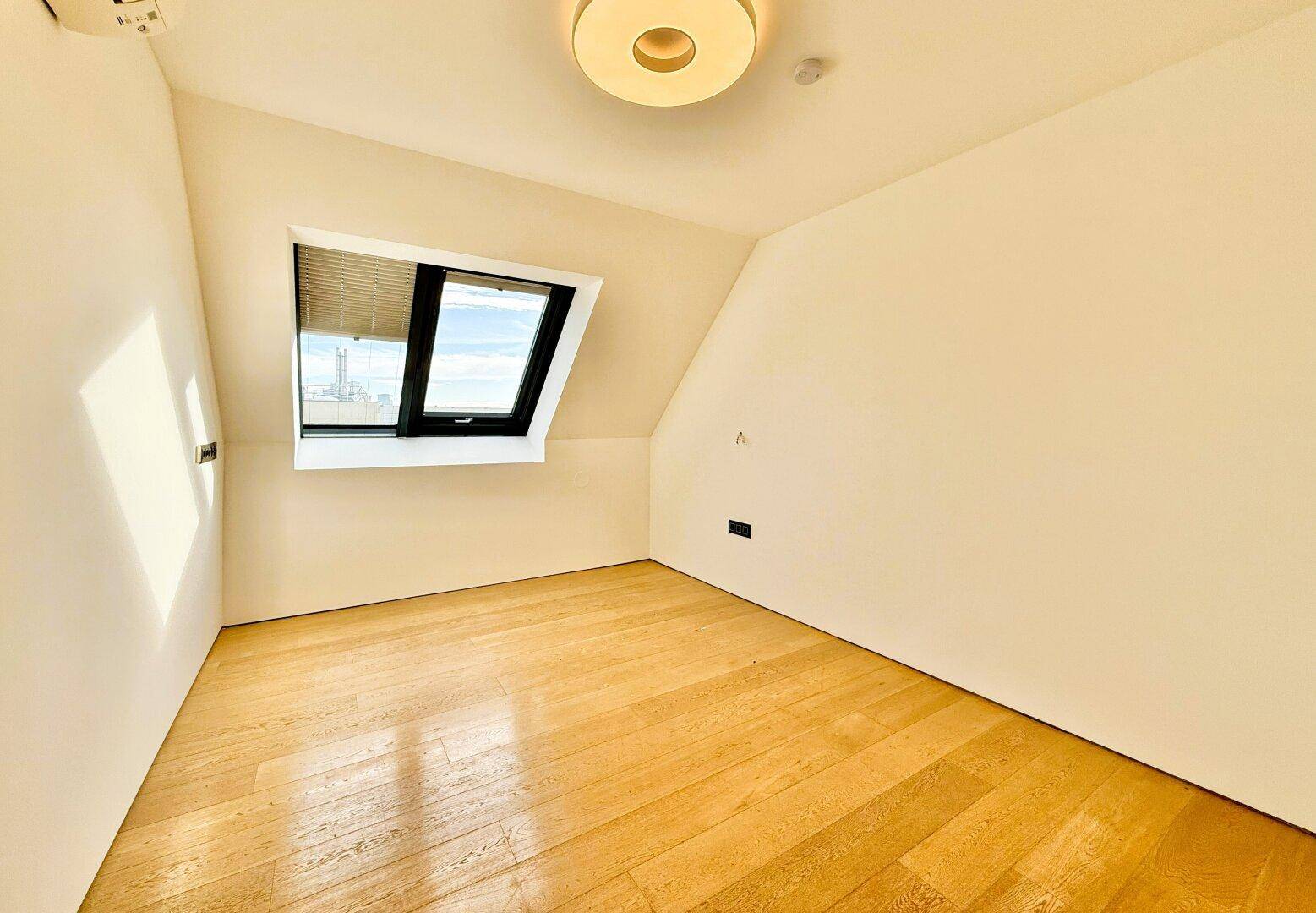 Helles, leeres Schlafzimmer mit Holzboden und Dachfenster, bietet eine ruhige und einladende Atmosphäre.