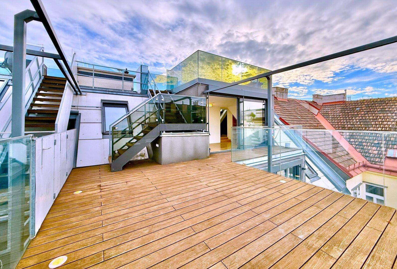 Weitläufige Dachterrasse mit Holzbelag und Glasgeländer, bietet einen beeindruckenden Blick auf die Stadt.