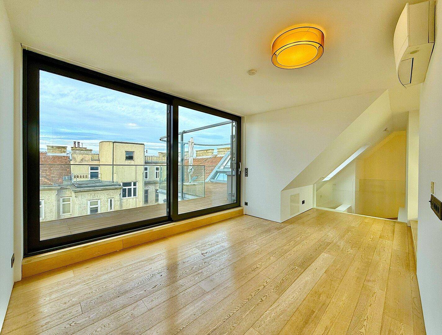 Helles, leeres Wohnzimmer mit Holzboden, großen Schiebetüren und schräger Decke, bereit zur individuellen Gestaltung.