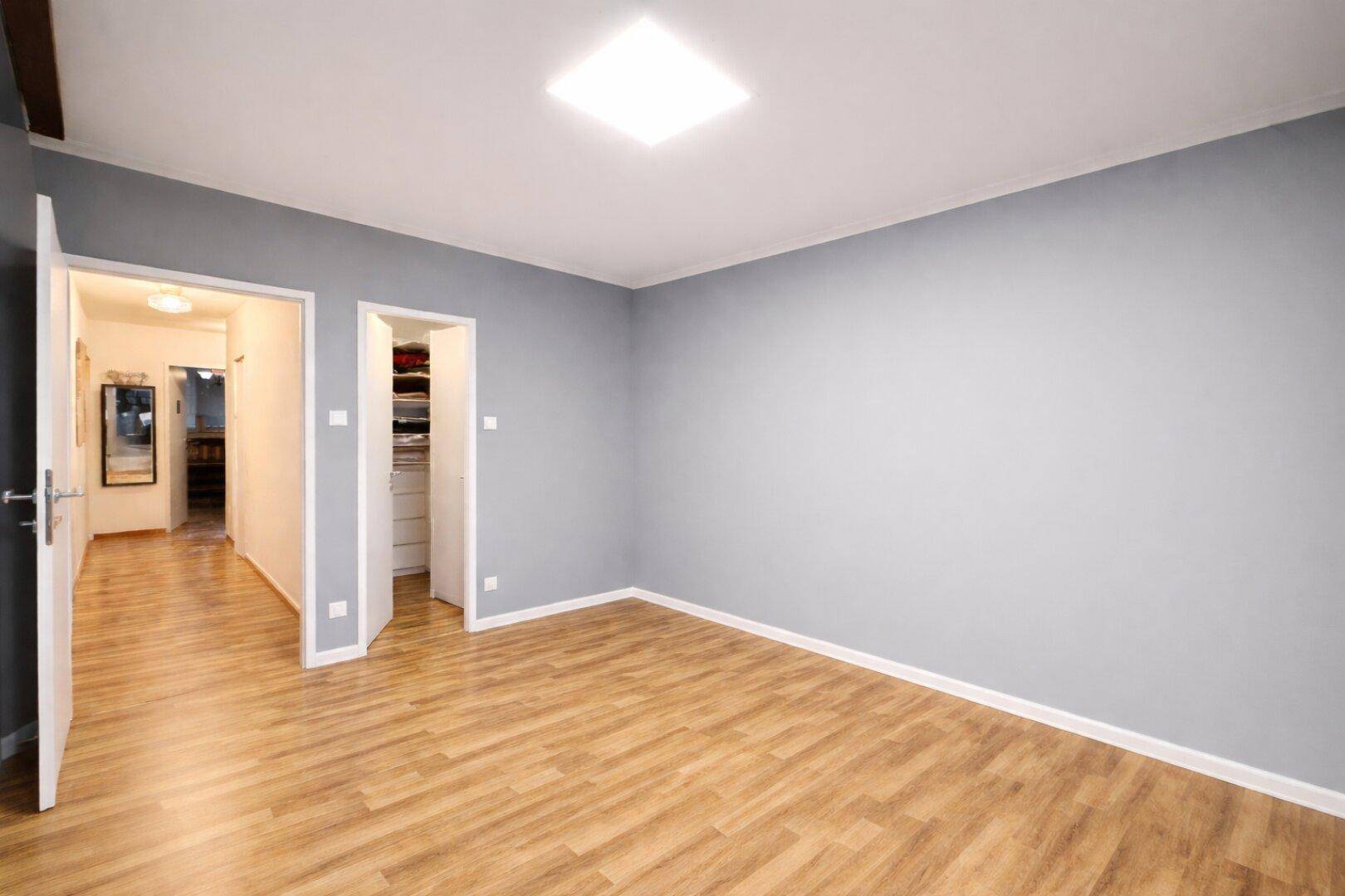 Heller Raum mit grauen Wänden, Laminatboden und Zugang zu Flur und Schrank.