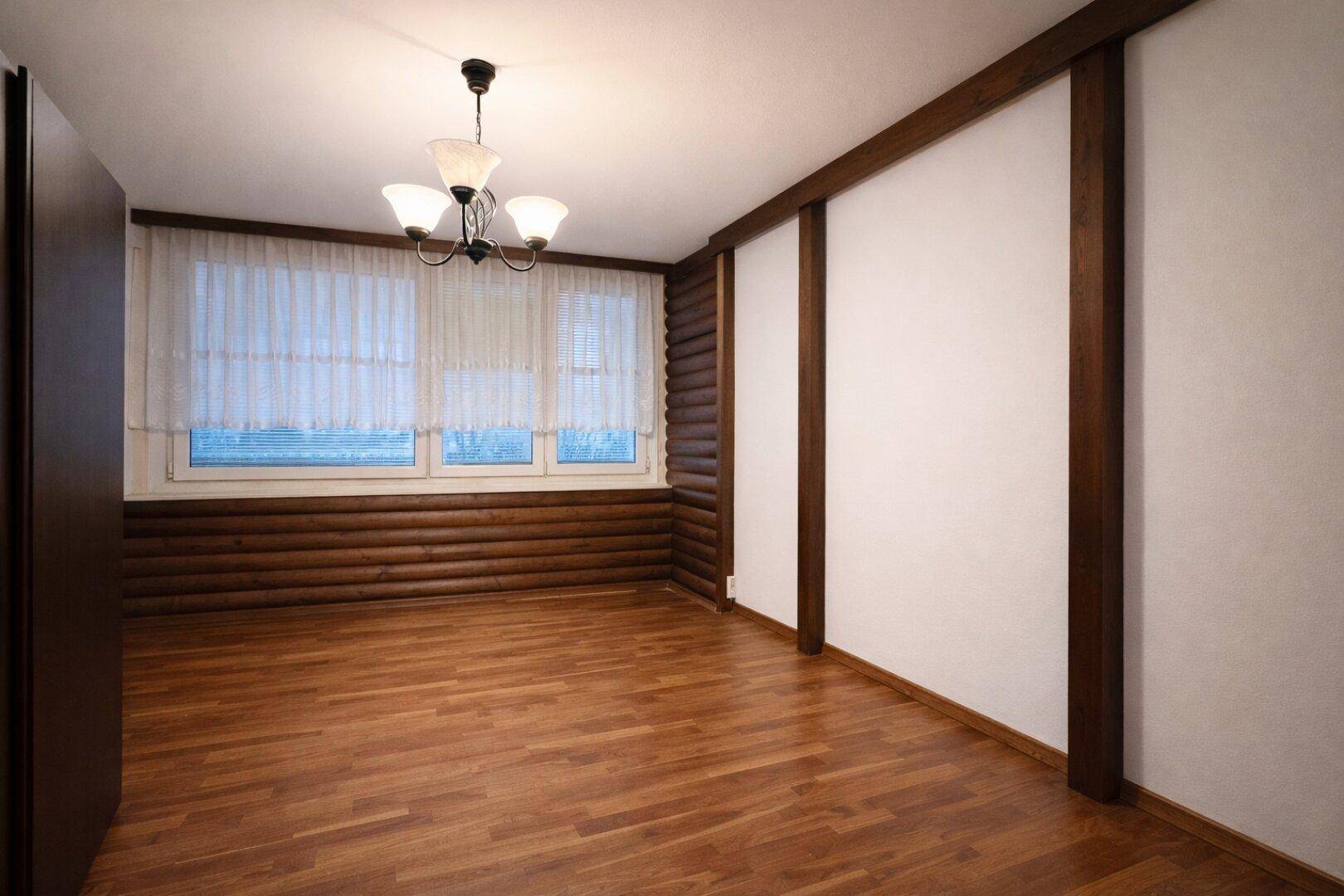Leerer Raum mit Holzwänden, Holzboden und einem Fenster, ideal als Schlafzimmer.