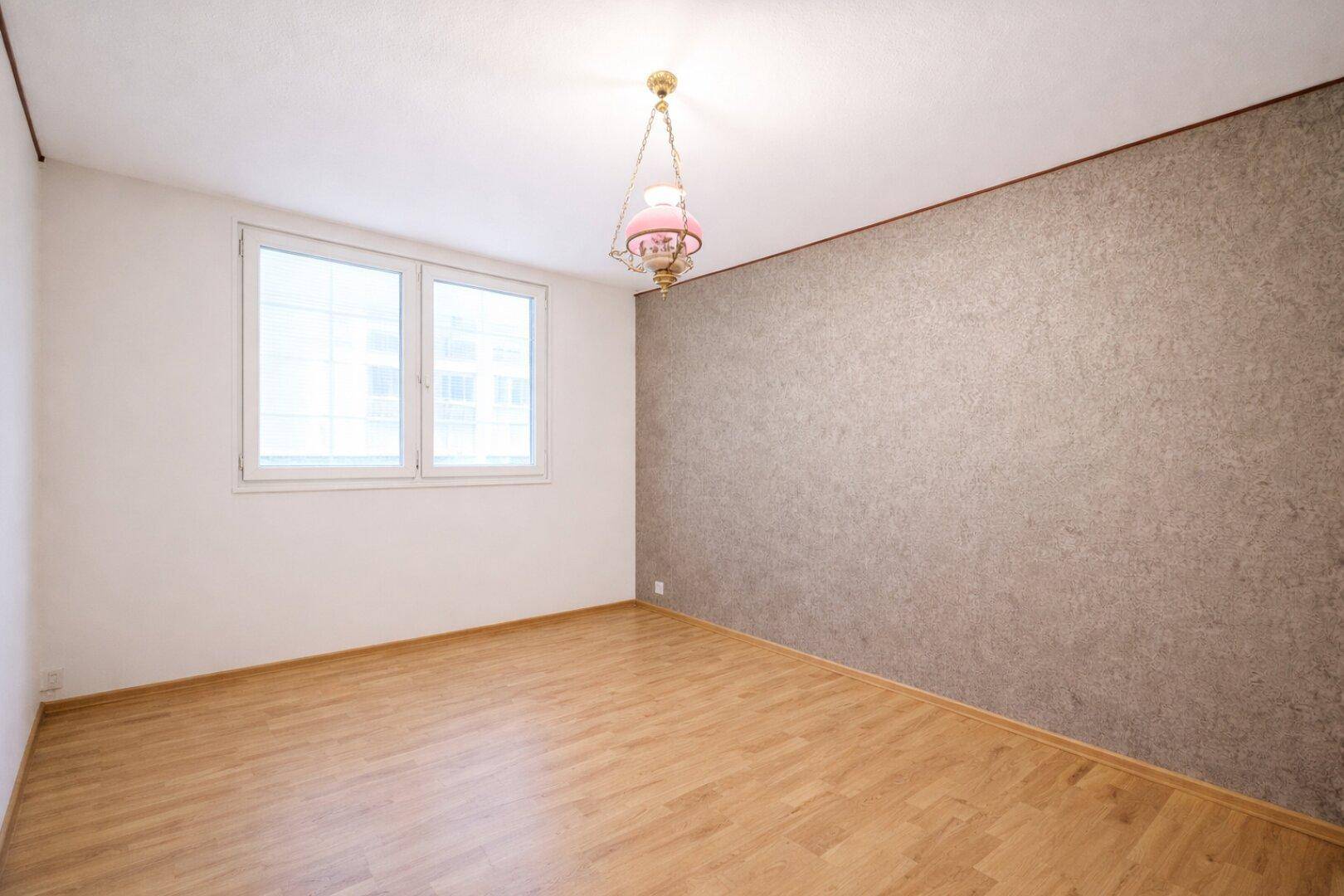 Leerer Raum mit Holzboden und einer strukturierten grauen Akzentwand.