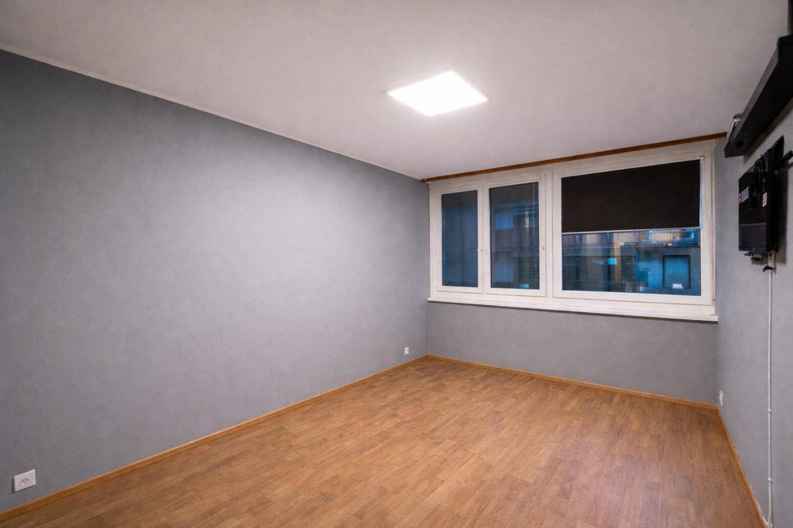 Leerer Raum mit grauen Wänden und hellem Laminatboden, ideal als Büro.