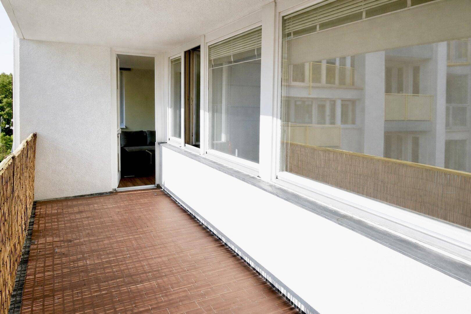 Balkon mit braunen Fliesen und Bambussichtschutz, mit Zugang zum Innenbereich.