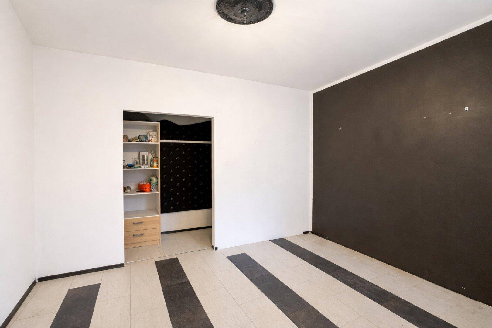 Unmöblierter Raum mit begehbarem Kleiderschrank und dunkler Akzentwand, bereit zur individuellen Gestaltung.