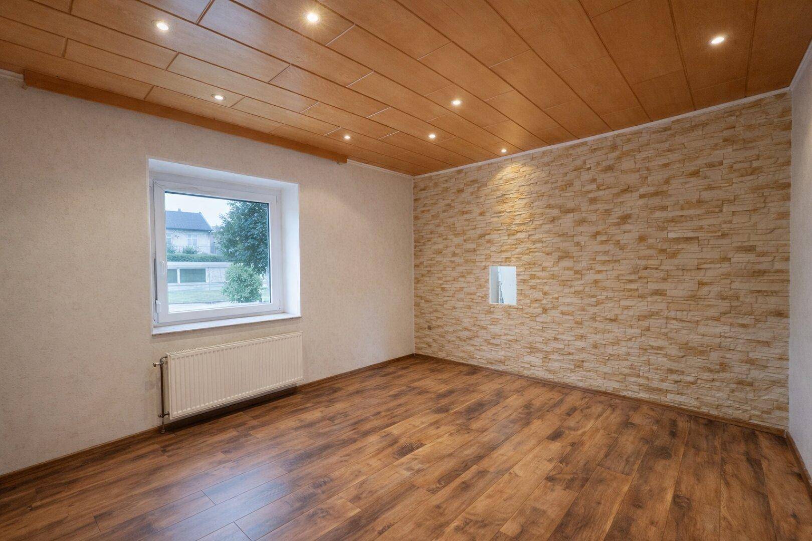 Unmöblierter Essbereich mit Laminatboden, Holzdecke und einer dekorativen Steinwand.