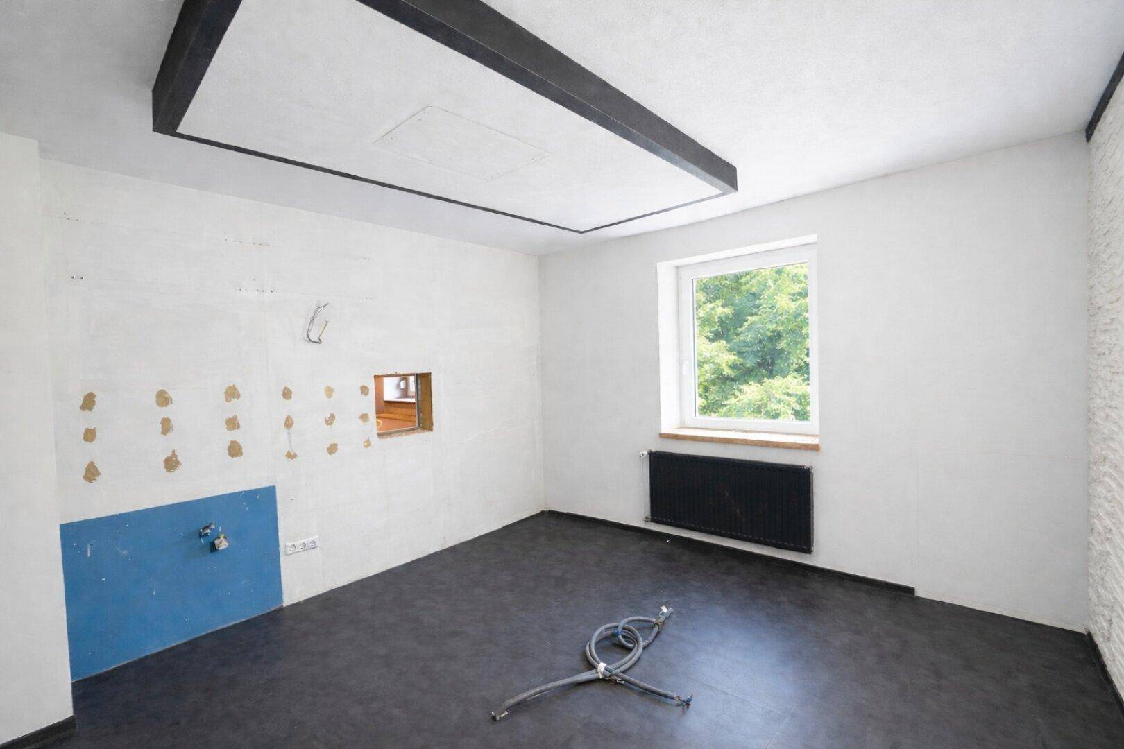 Leerer Küchenraum mit Anschlüssen und Fenster, bereit für die Installation einer neuen Einbauküche.