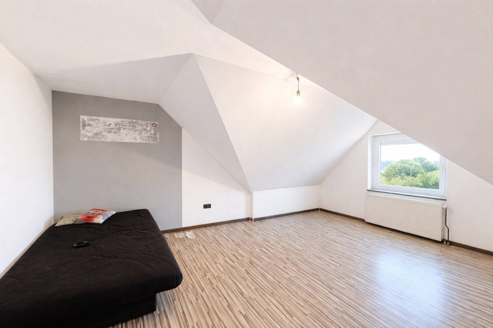 Helles Schlafzimmer im Dachgeschoss mit Schrägen, Holzboden und Fenster, ideal für ein Kinderzimmer.