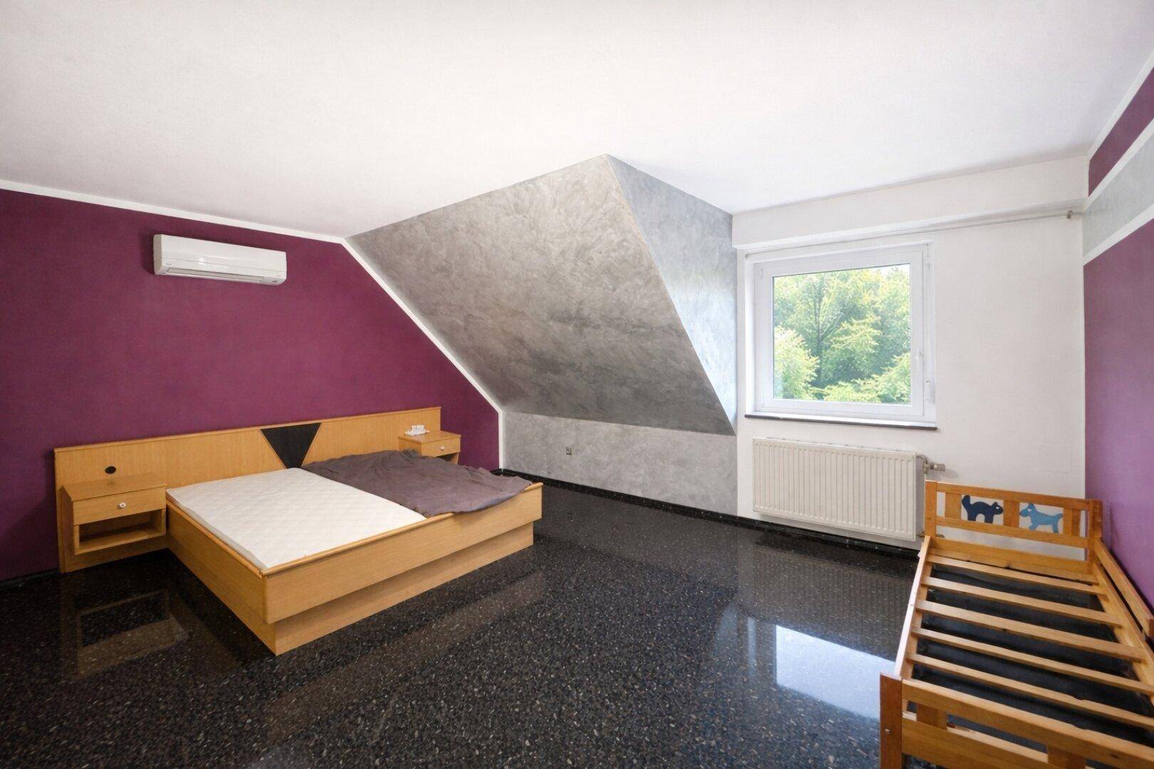 Unmöbliertes Schlafzimmer im Dachgeschoss mit Schrägen, Klimaanlage und Fenster mit Blick ins Grüne.