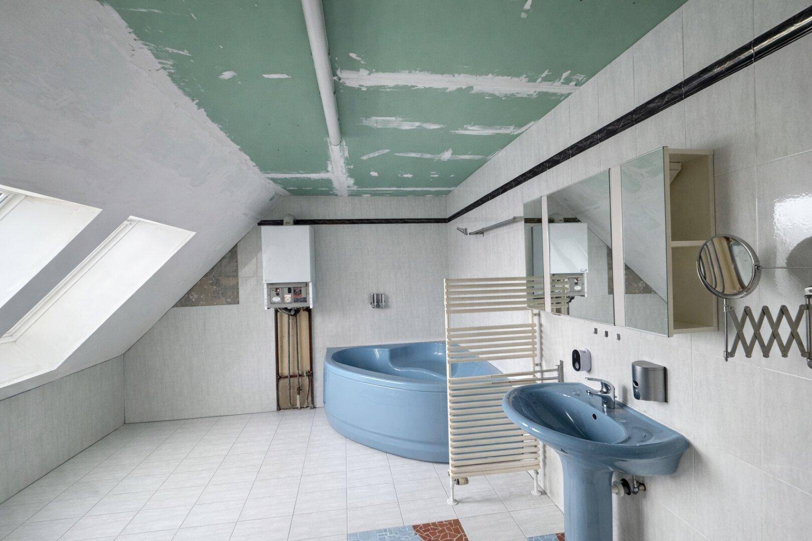Badezimmer im Dachgeschoss mit blauer Eckbadewanne, Heizkörper und Dachfenstern, renovierungsbedürftig.