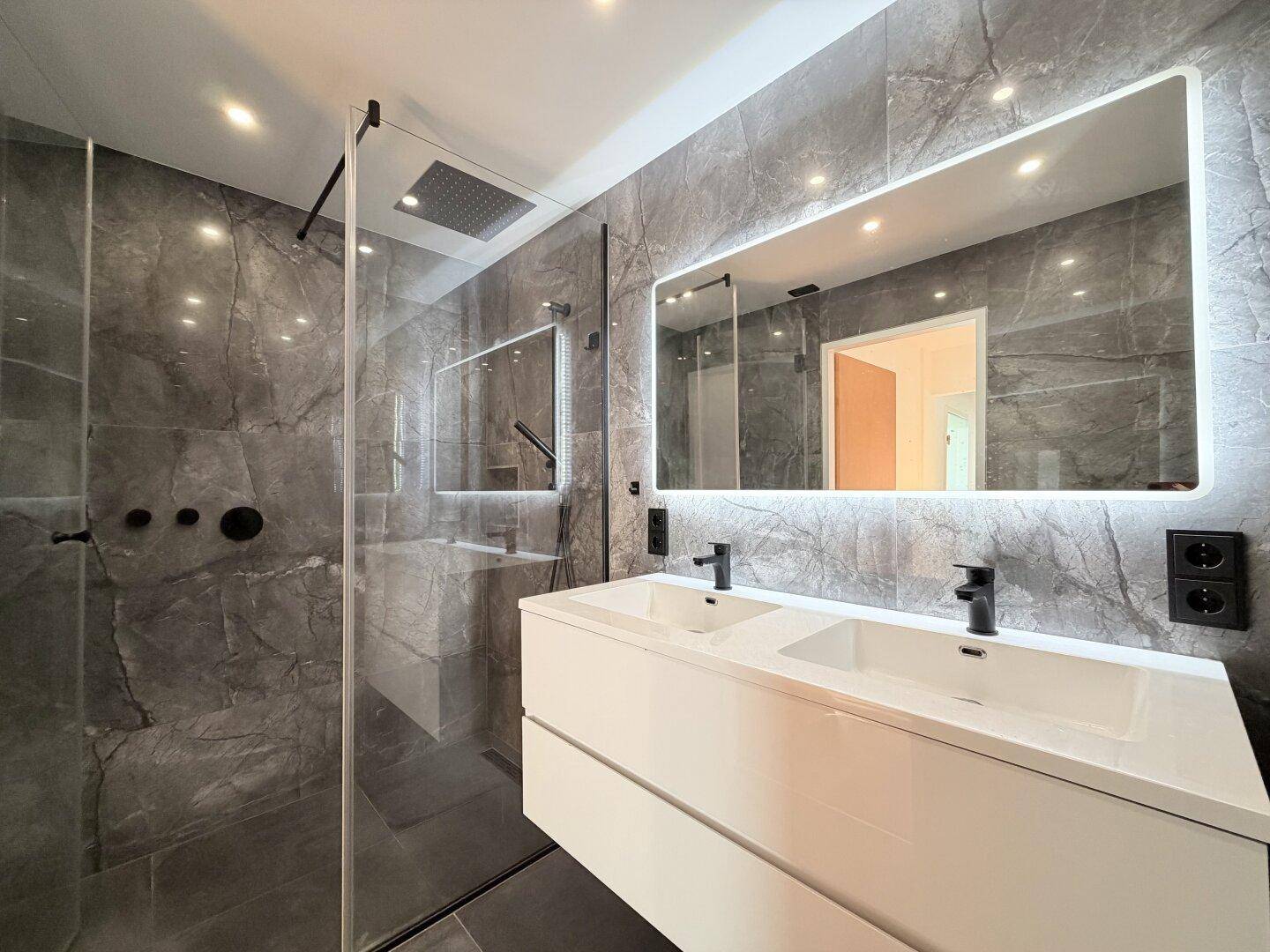 Modernes Badezimmer mit grauen Marmorfliesen, Doppelwaschbecken und großer Regendusche.
