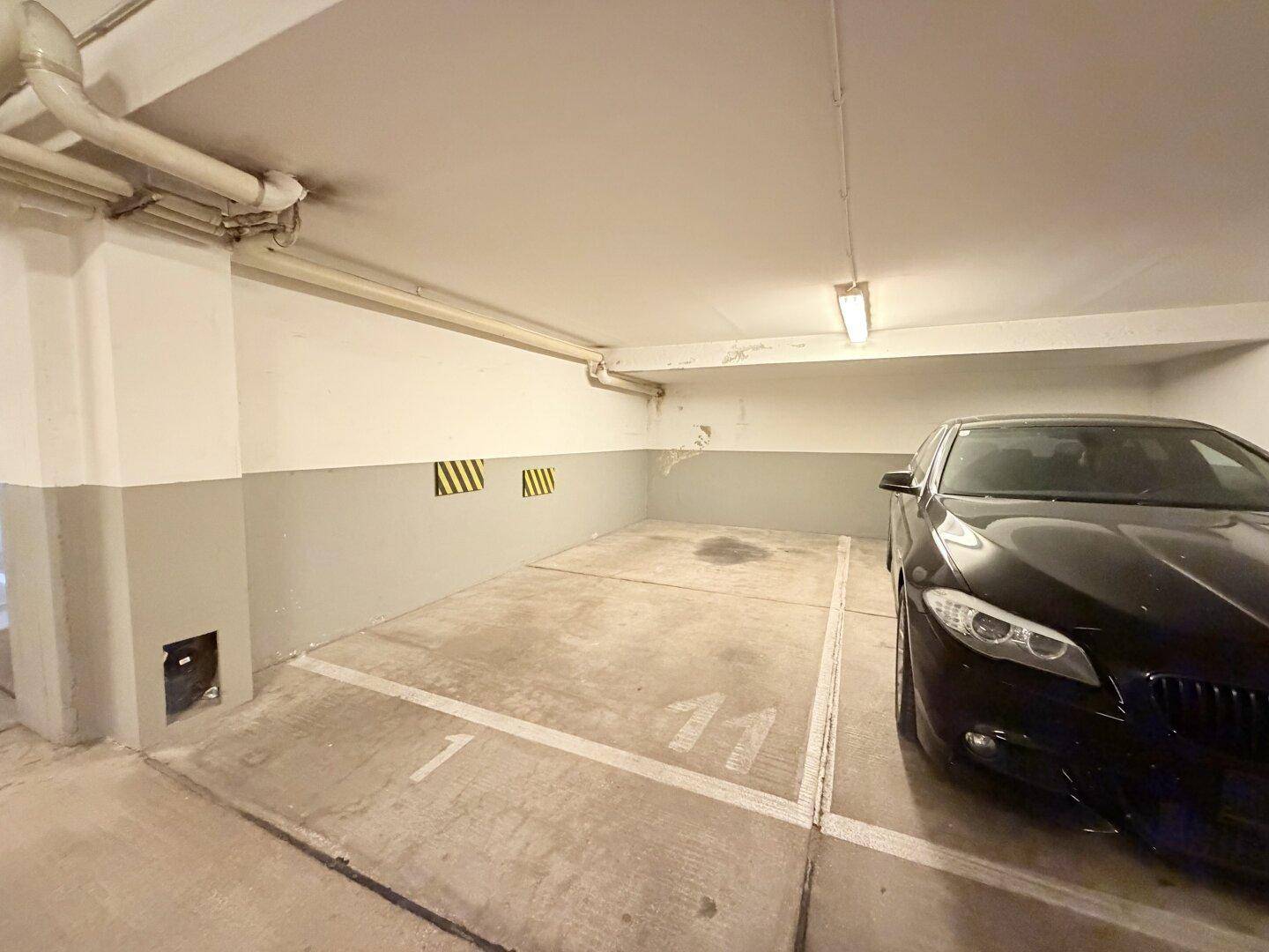 Tiefgaragenstellplatz mit Betonboden und einem geparkten schwarzen Auto.