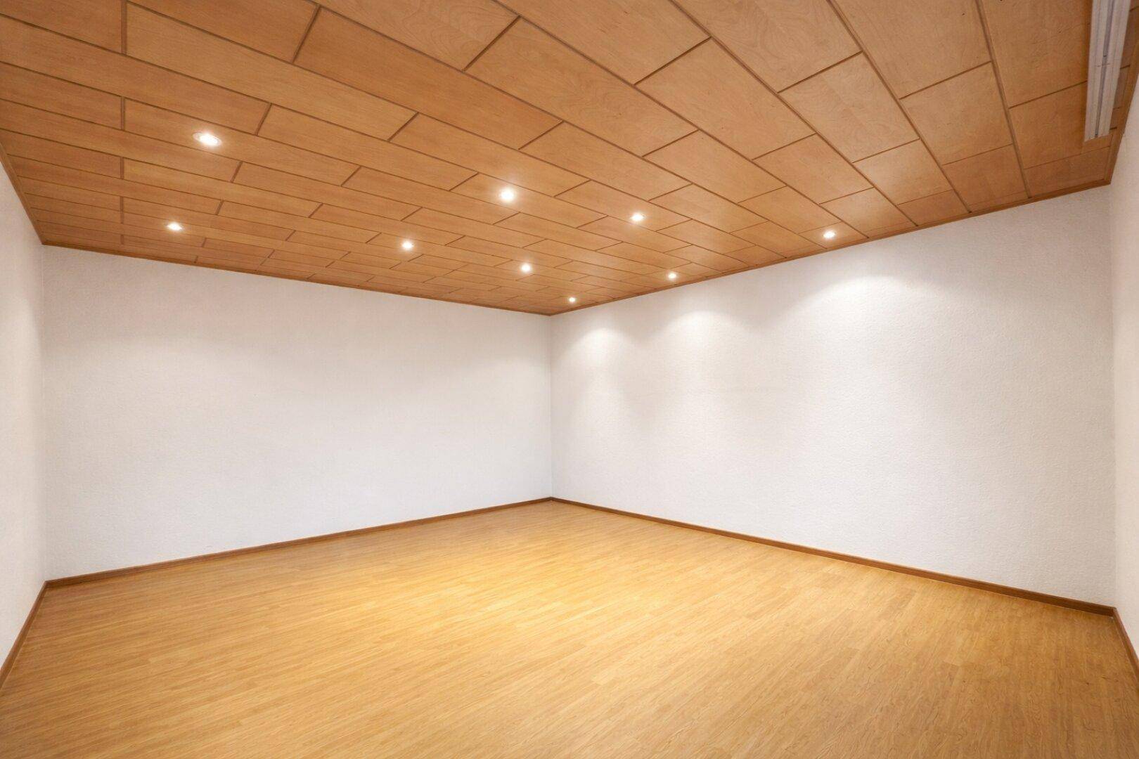 Geräumiges, unmöbliertes Wohnzimmer mit hellem Holzboden und Holzpaneeldecke, bereit zur Einrichtung.