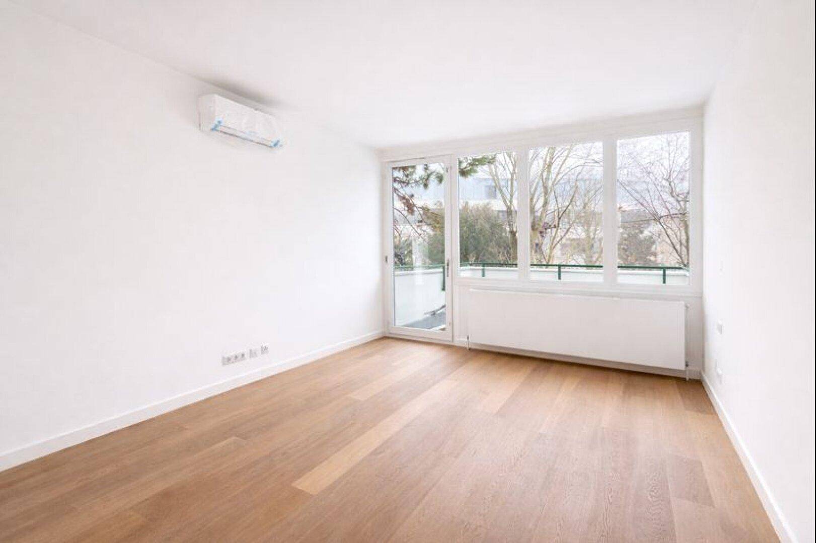 Leeres Schlafzimmer mit Holzboden, großen Fenstern und Klimaanlage.