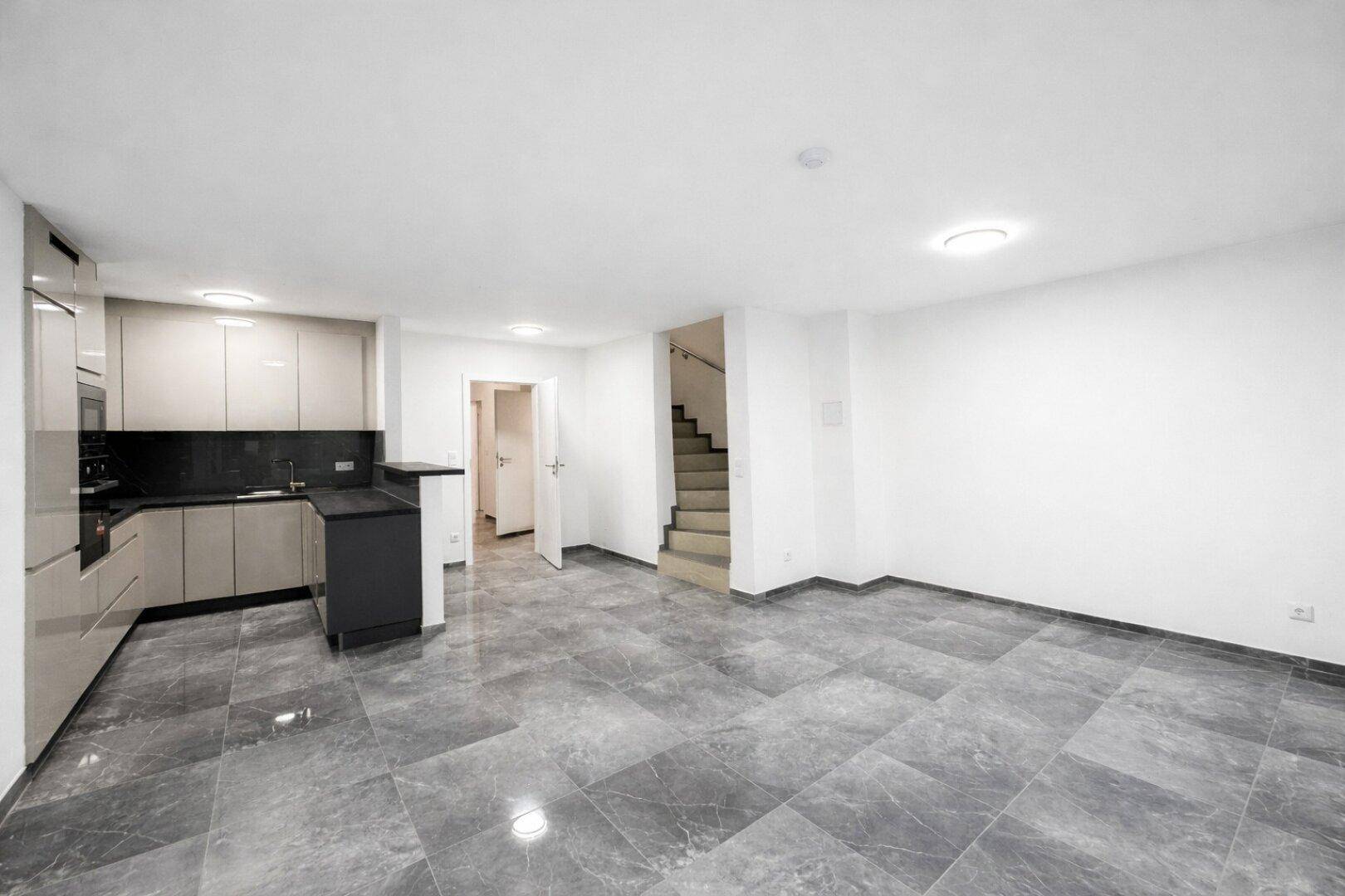 Leerer offener Wohn-Essbereich mit moderner Einbauküche und Zugang zur Treppe.