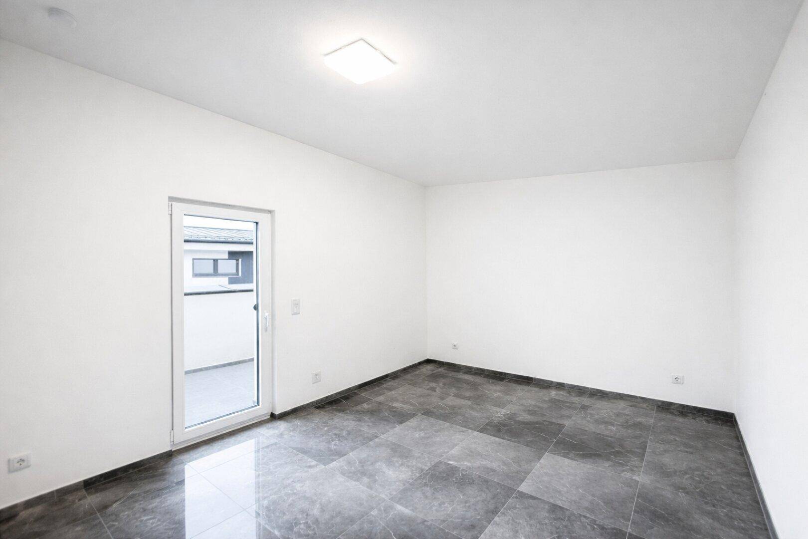 Leeres Schlafzimmer mit Fliesenboden und Tür zu einem potenziellen Balkon oder Terrasse.