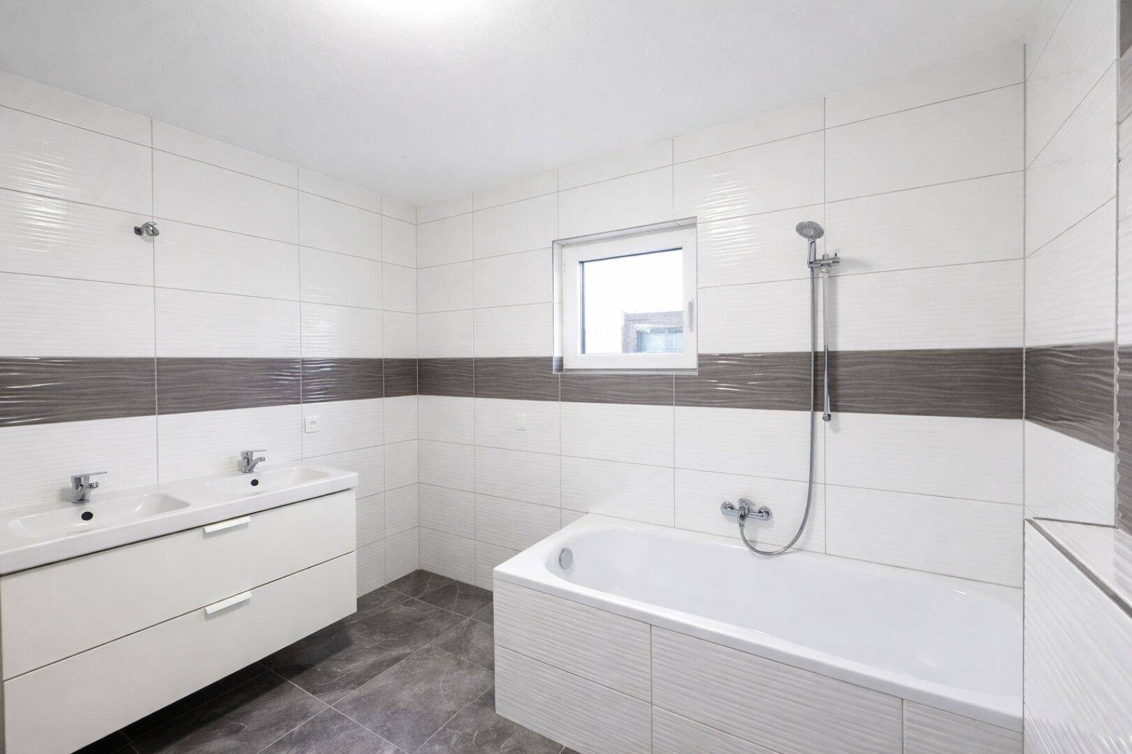 Modernes Badezimmer mit Badewanne, Doppelwaschbecken und Fenster für Tageslicht.