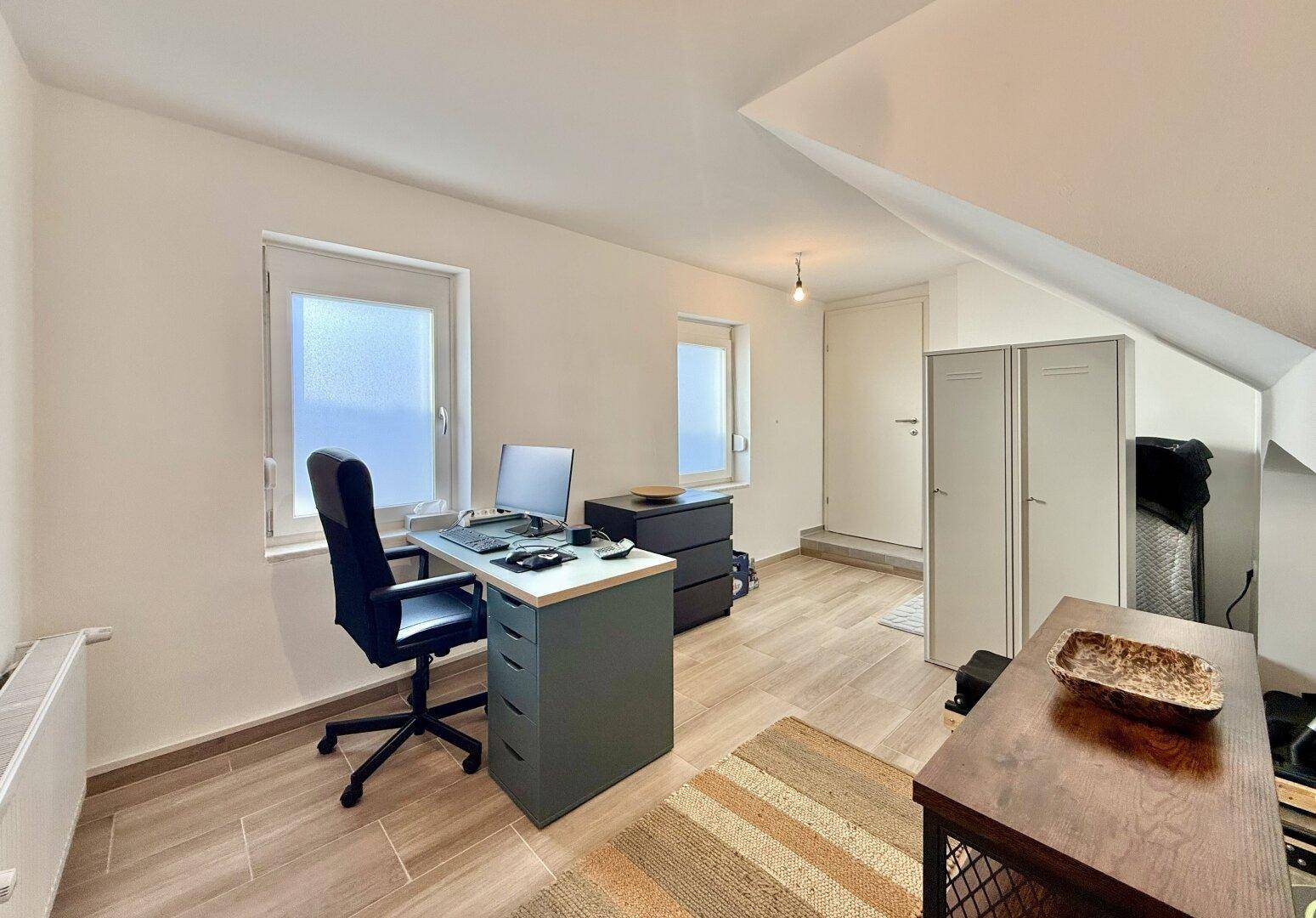 Helles Büro im Dachgeschoss mit Schreibtisch, Schränken und schrägen Decken.