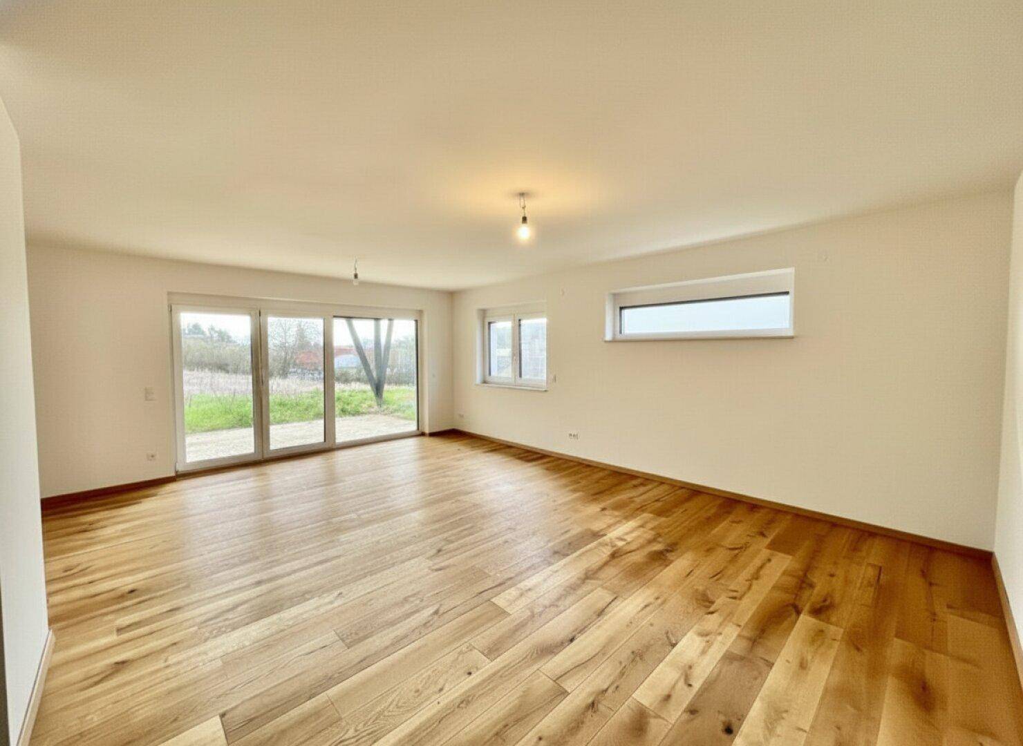 Geräumiges, leeres Wohnzimmer mit Holzboden und großen Fenstern für viel Tageslicht.