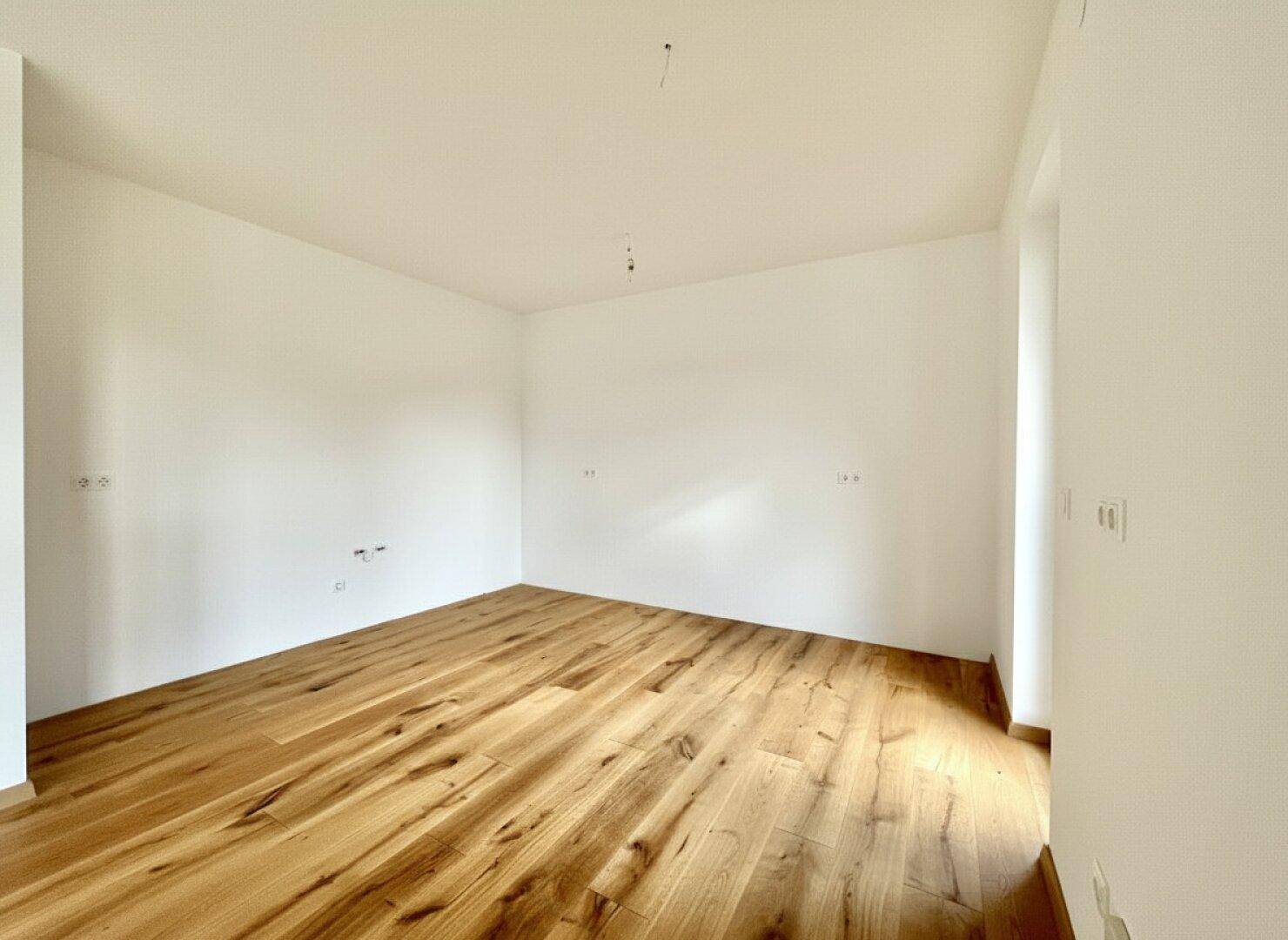 Geräumiger, leerer Küchenbereich mit Holzboden, bereit für die Installation einer Einbauküche.
