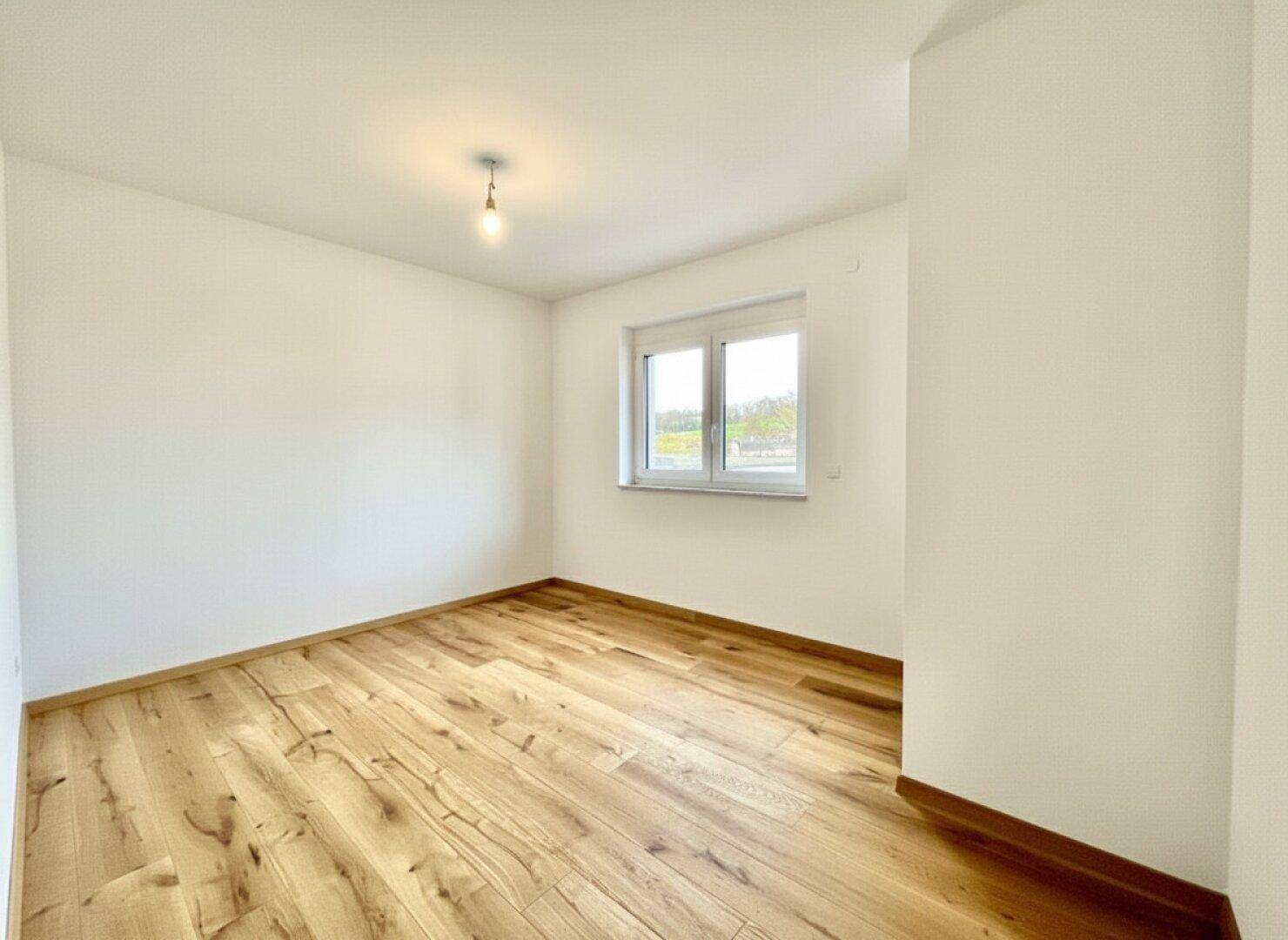Helles, leeres Schlafzimmer mit Holzboden und großem Fenster, ideal für ein Kinderzimmer.