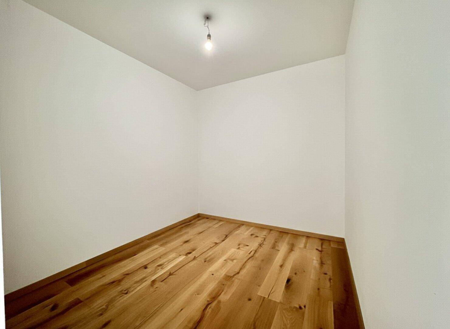 Kleiner, heller Raum mit Holzboden und Fenster, vielseitig nutzbar als Abstellraum oder Ankleidezimmer.