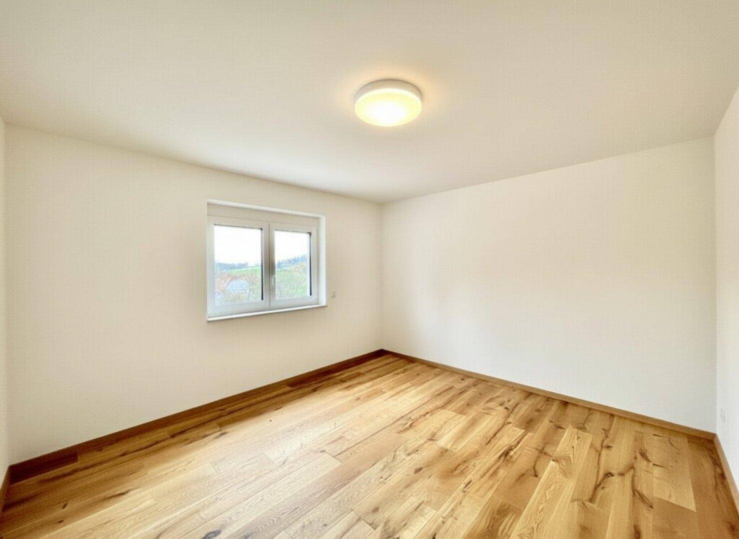 Helles, leeres Zimmer mit Holzboden und Fenster, vielseitig nutzbar als Schlaf- oder Arbeitszimmer.