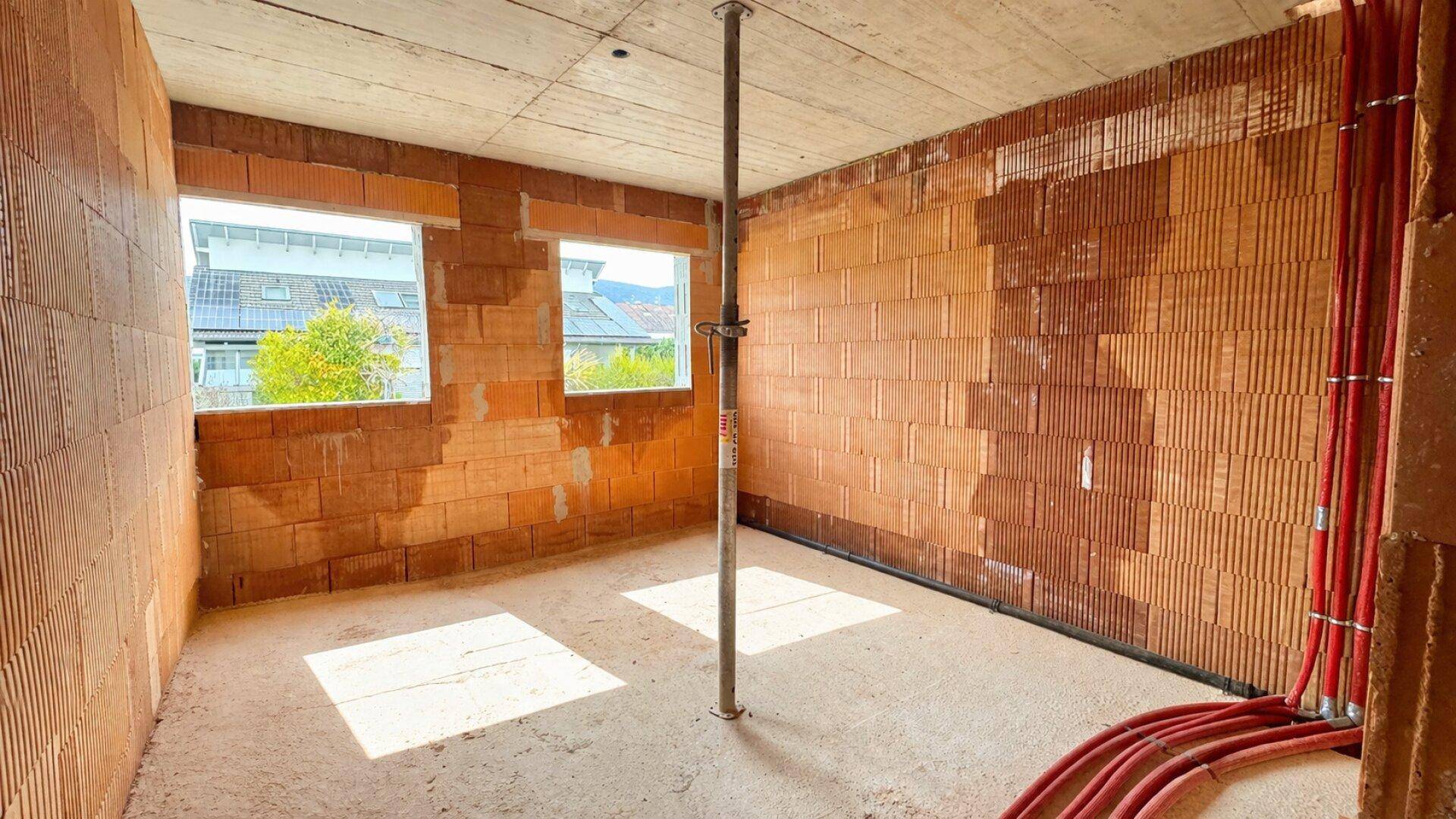 Innenraum im Rohbau mit Ziegelwänden, Betonboden und sichtbaren Rohrleitungen.