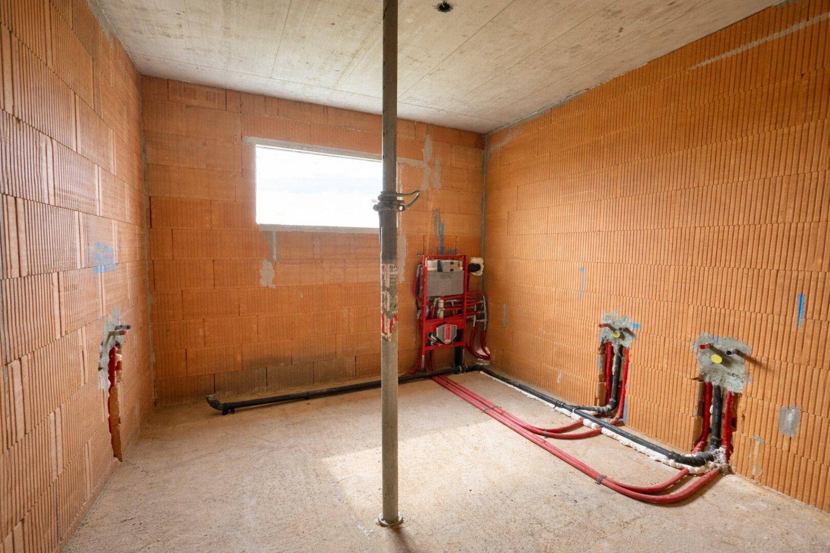 Rohbau eines Badezimmers oder WCs mit sichtbaren Wasserinstallationen und Ziegelwänden.