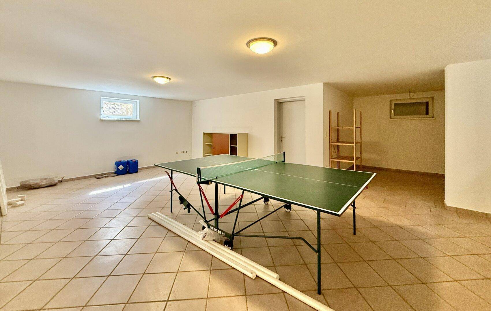 Großer Hobbyraum im Keller mit Fliesenboden und Tischtennisplatte, ideal für Freizeitaktivitäten.