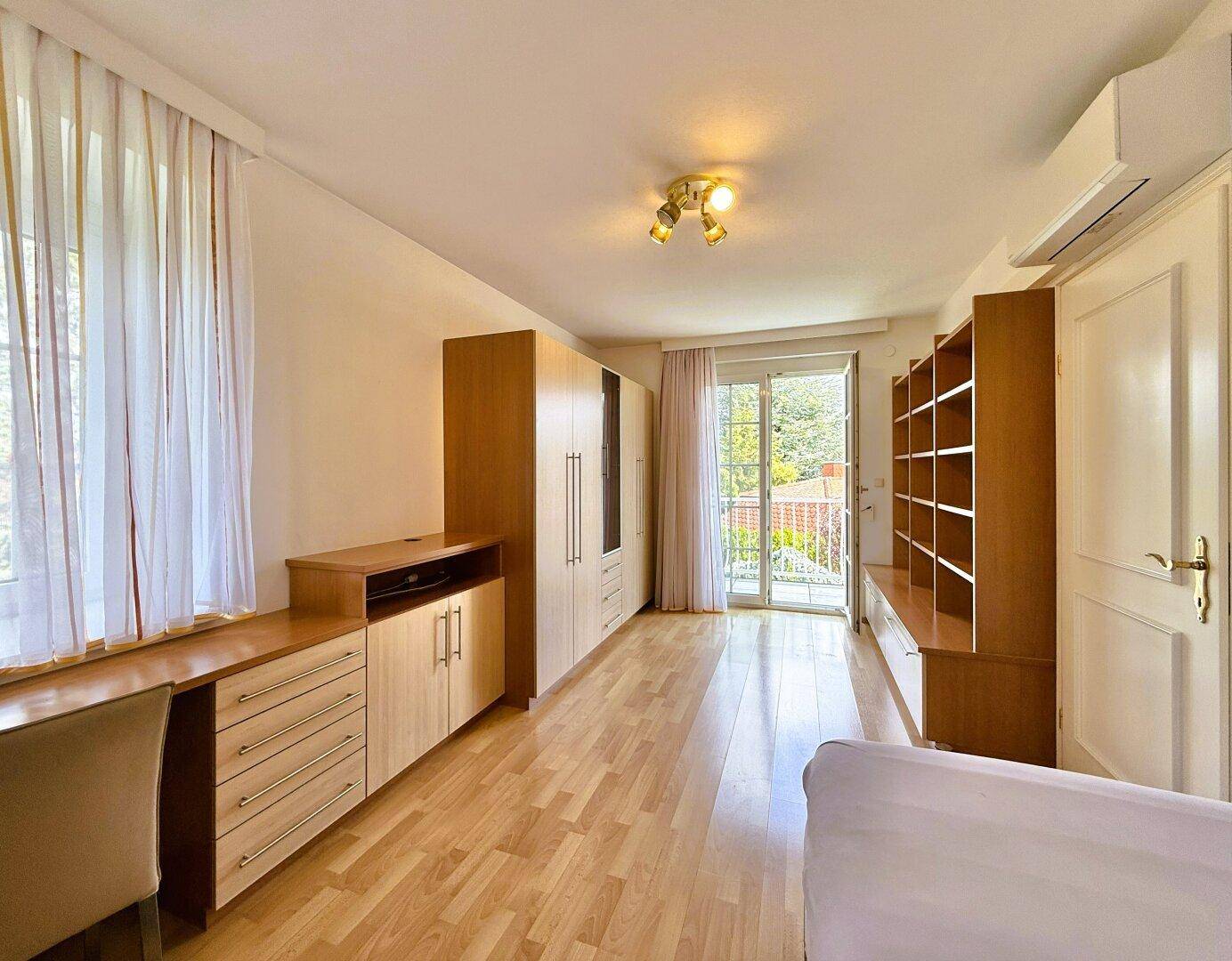 Schlafzimmer mit Holzfußboden, Einbauschränken und Balkonzugang für frische Luft.