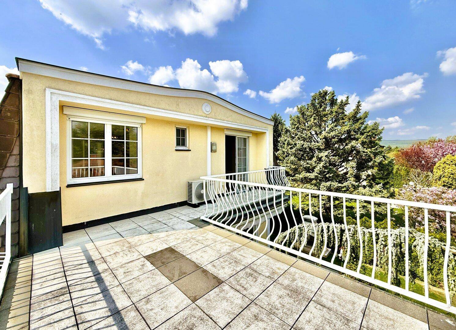 Große geflieste Terrasse mit weißem Geländer und weitem Blick über die umliegende Landschaft.