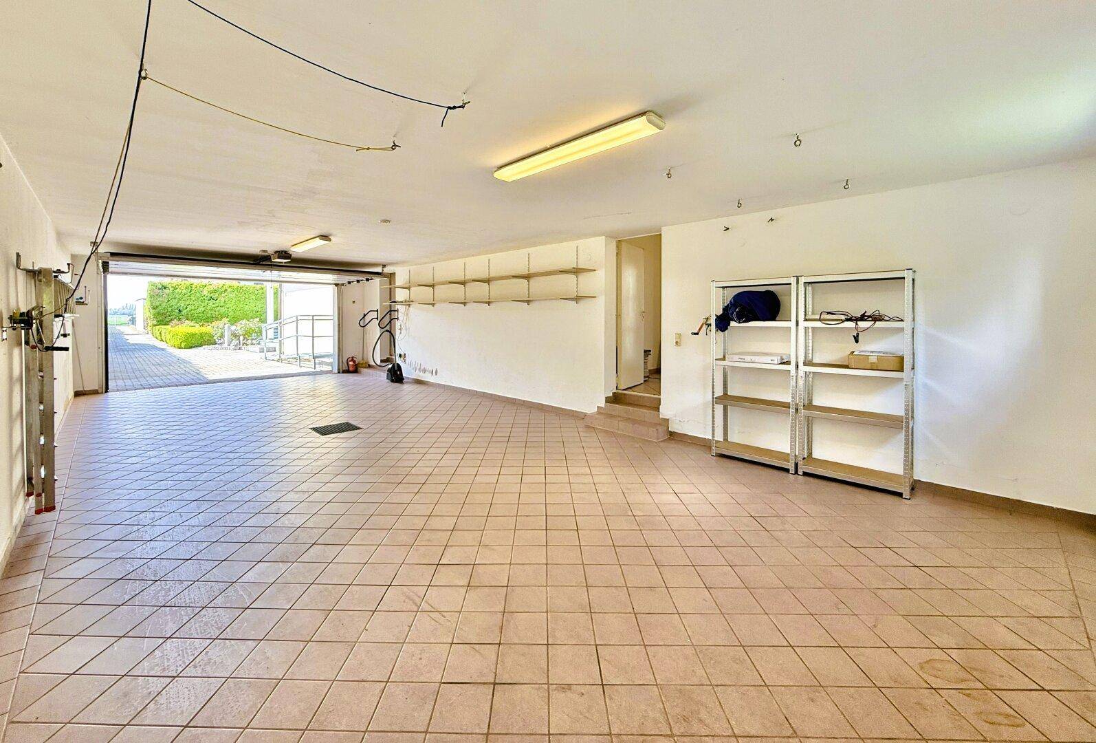 Geräumige Garage mit Fliesenboden, Regalen und direktem Zugang zum Außenbereich.
