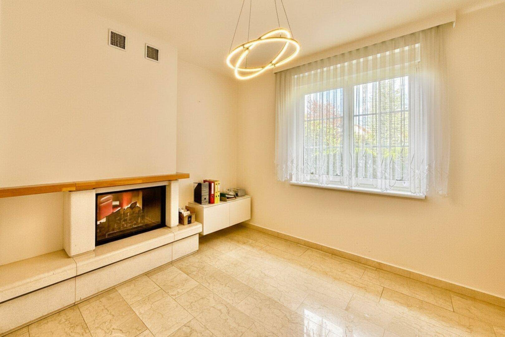 Helles Arbeitszimmer mit Kamin, Marmorboden und großem Fenster mit Blick ins Grüne.