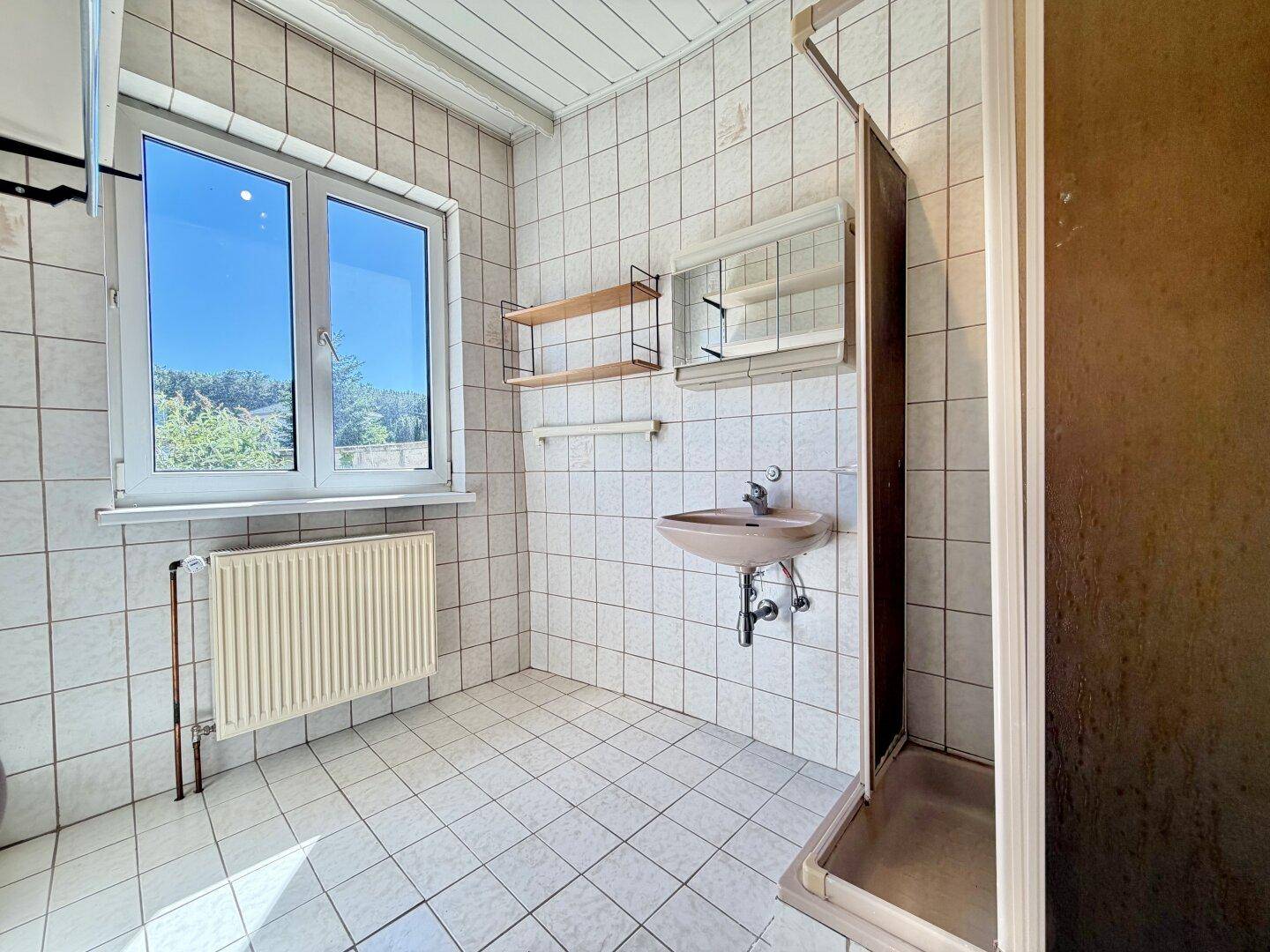 Einfaches Badezimmer mit Fliesen, Fenster und Duschkabine, funktional und hell.