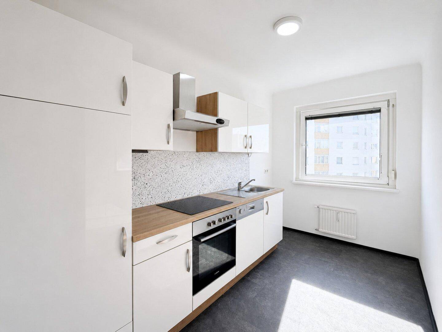 Helle Einbauküche mit weißen Schränken, Holz-Arbeitsplatte und modernen Geräten.