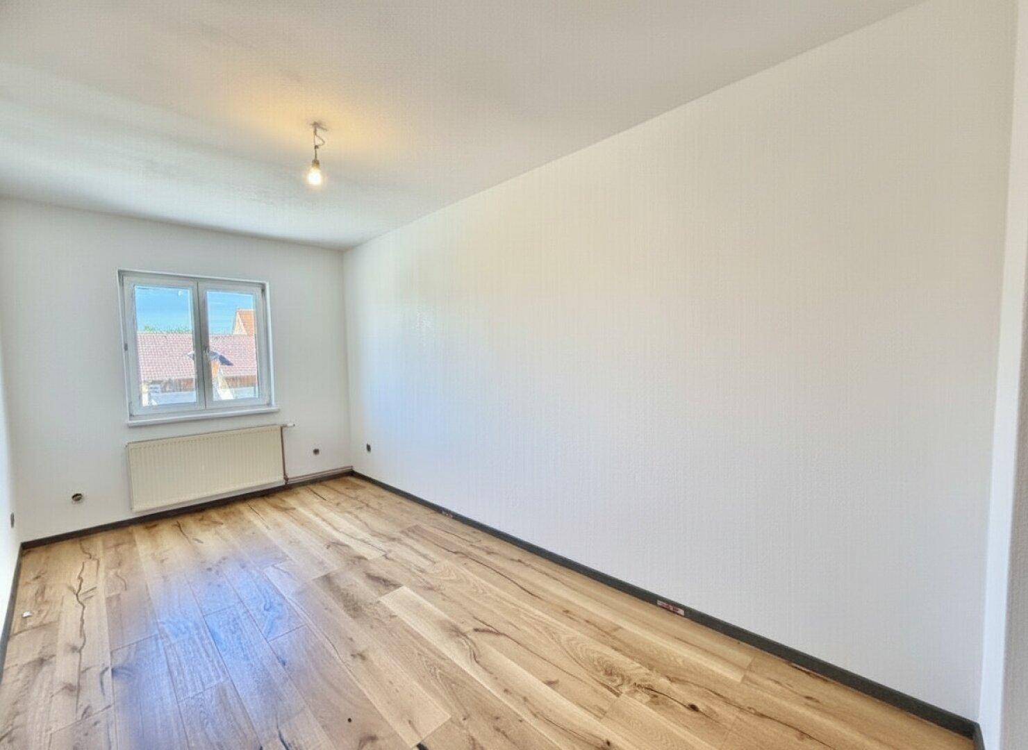 Leeres, helles Schlafzimmer mit Holzboden und Fenster, bereit für neue Bewohner.