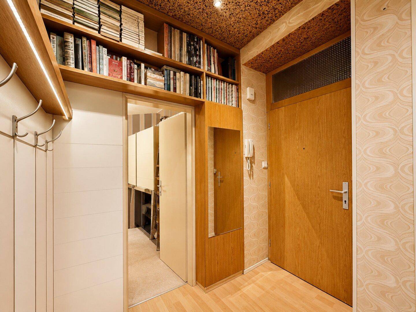 Flur mit Einbauregal, Garderobe und Holztüren, ausgestattet mit gemusterter Tapete.
