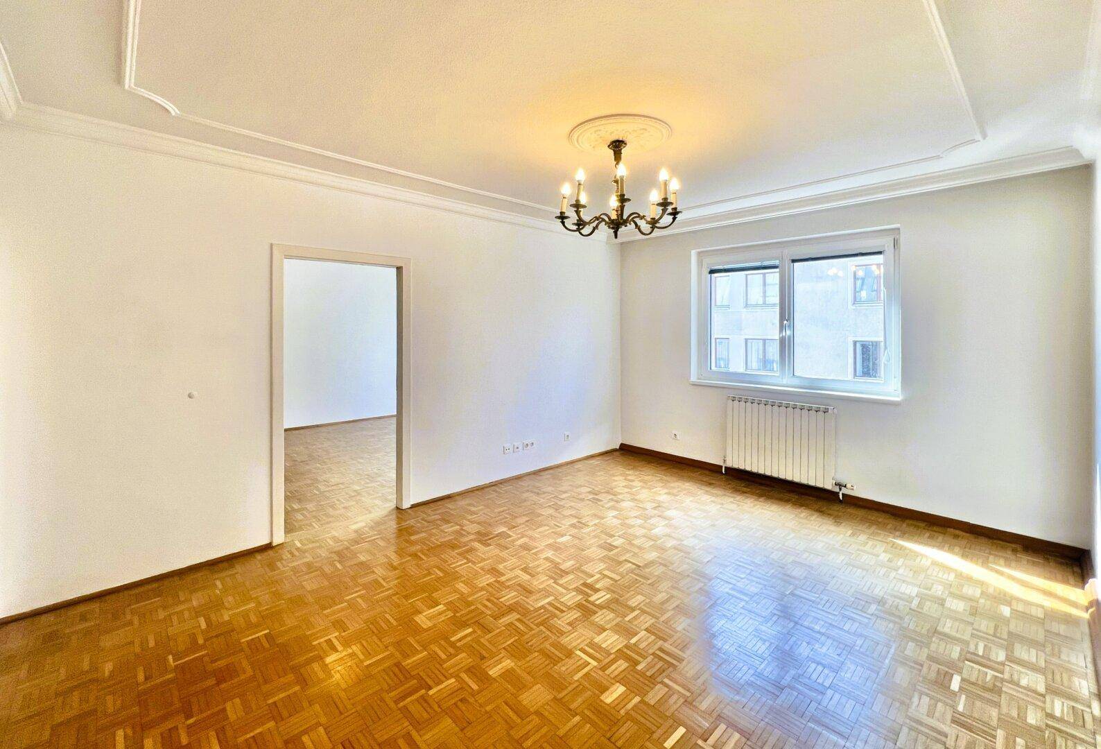 Leeres Schlafzimmer mit klassischem Parkettboden, Fenster und eleganter Stuckdecke.