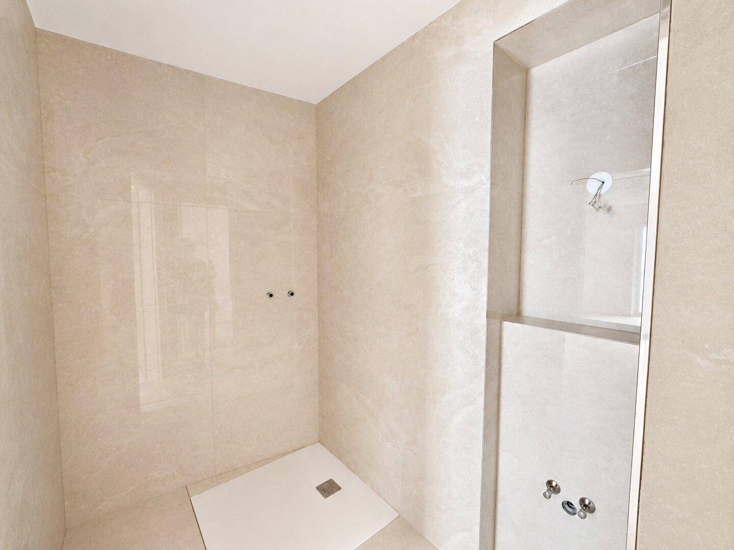 Unmöblierter Duschbereich in einem Badezimmer mit beigefarbenen Wand- und Bodenfliesen.
