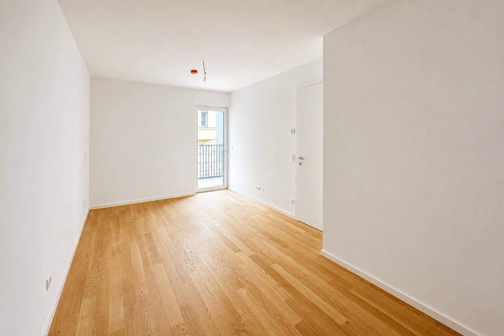 Unmöbliertes Kinderzimmer mit Holzboden und Zugang zu einem französischen Balkon.
