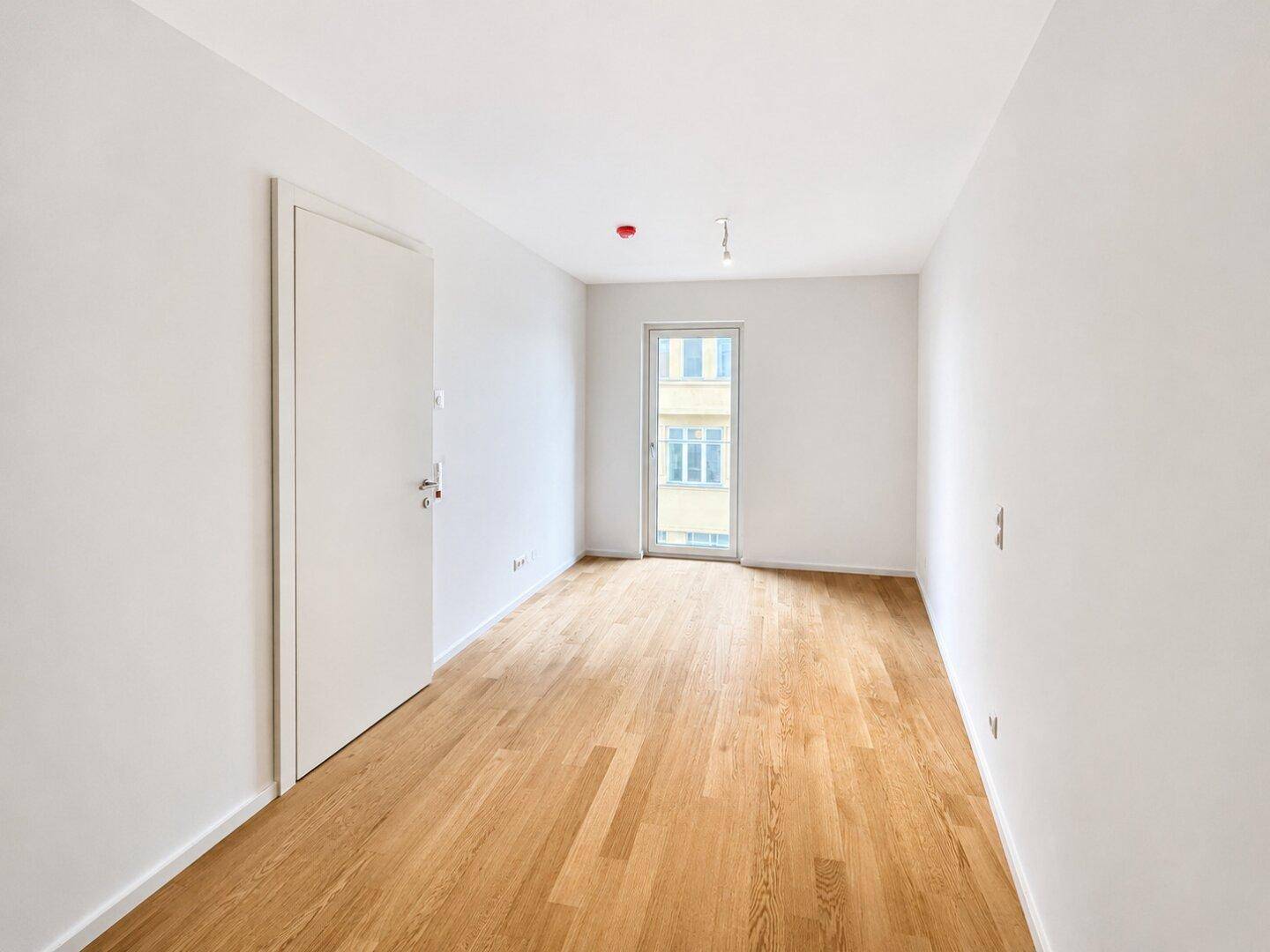 Unmöbliertes Schlafzimmer mit Holzboden und Zugang zu einem französischen Balkon.