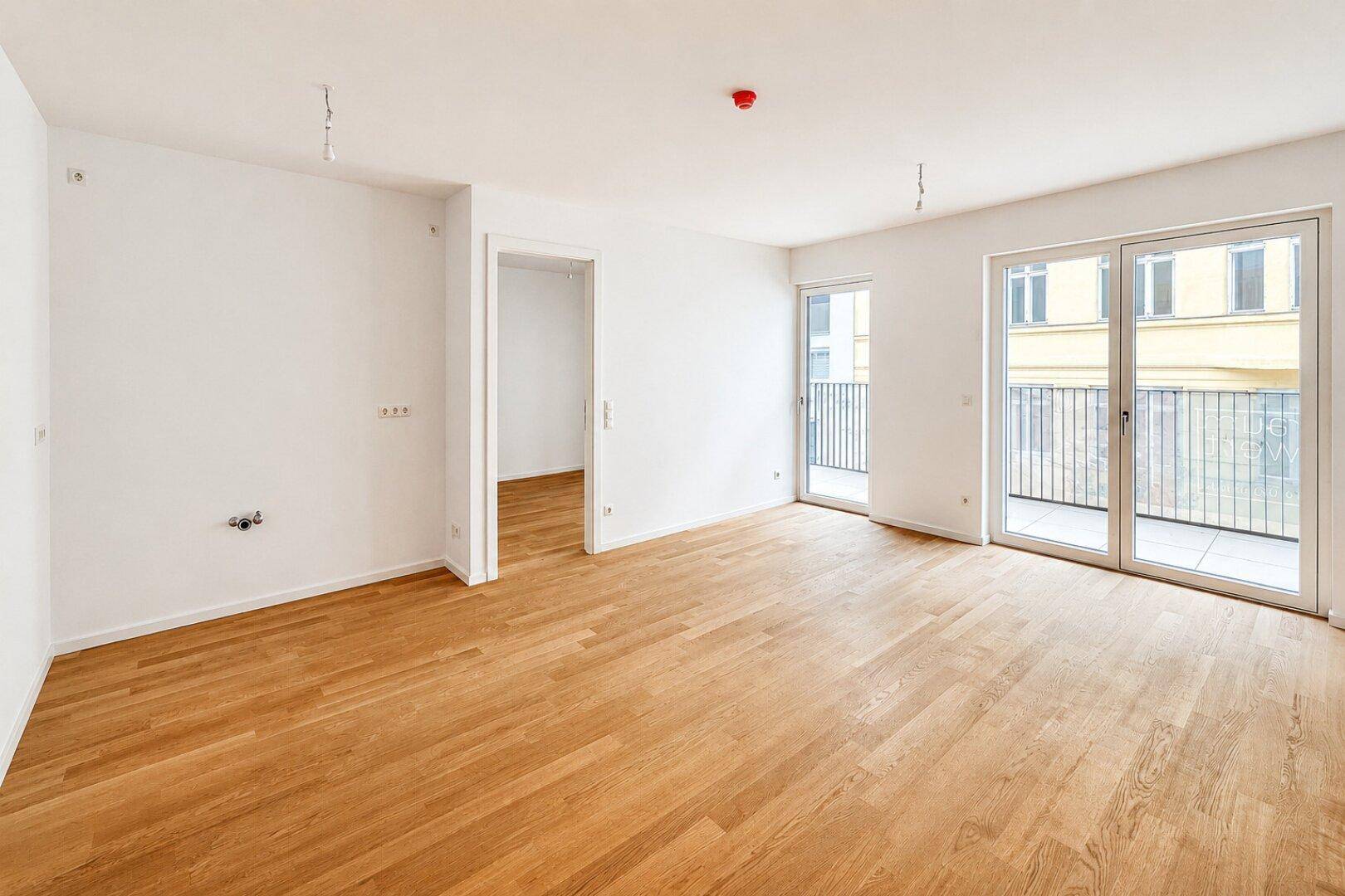 Heller, unmöblierter Wohnbereich mit Holzboden und großem Balkonzugang.