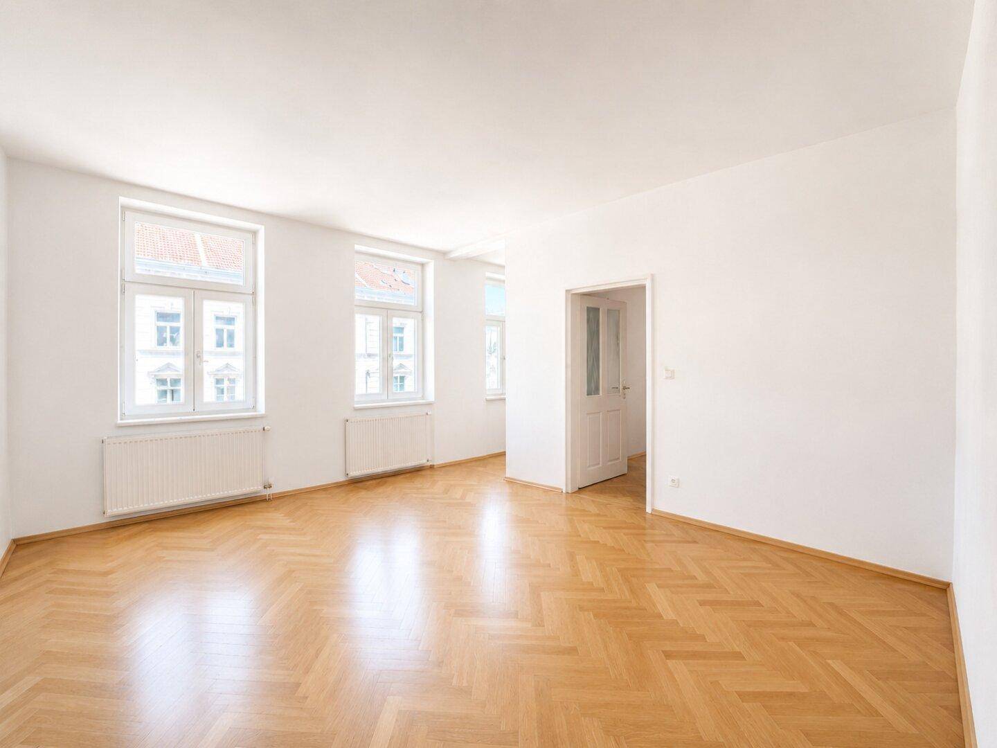 Geräumiges, leeres Zimmer mit Fischgrätparkett und großen Fenstern, bereit zur individuellen Gestaltung.