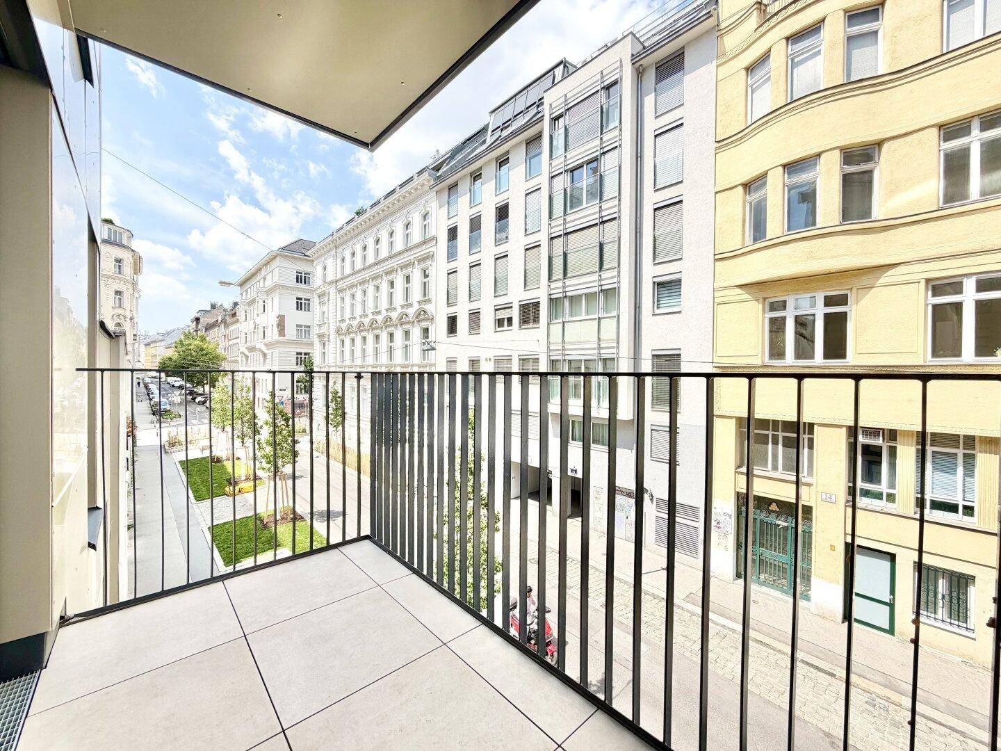 Heller Balkon mit Fliesenboden und Metallgeländer, bietet einen Blick auf die Stadtstraße.