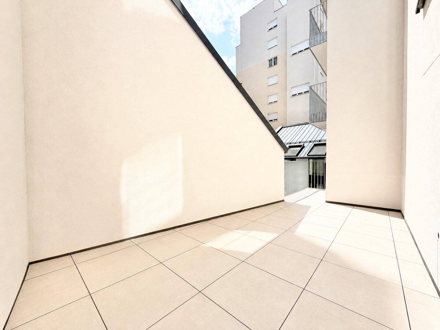 Leere Terrasse mit hellen Fliesen und hohen Wänden, bietet Raum für individuelle Gestaltung im Freien.